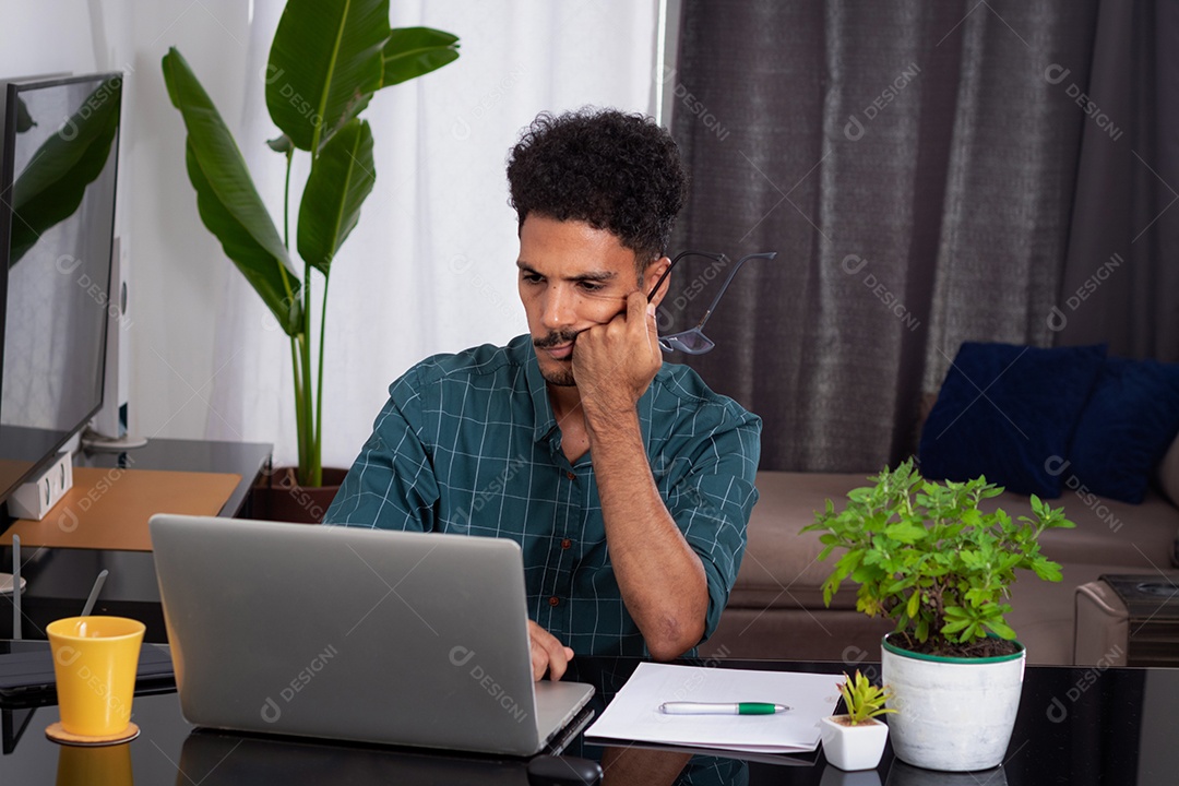 Jovem negro fazendo home office durante o dia na mesa com laptop