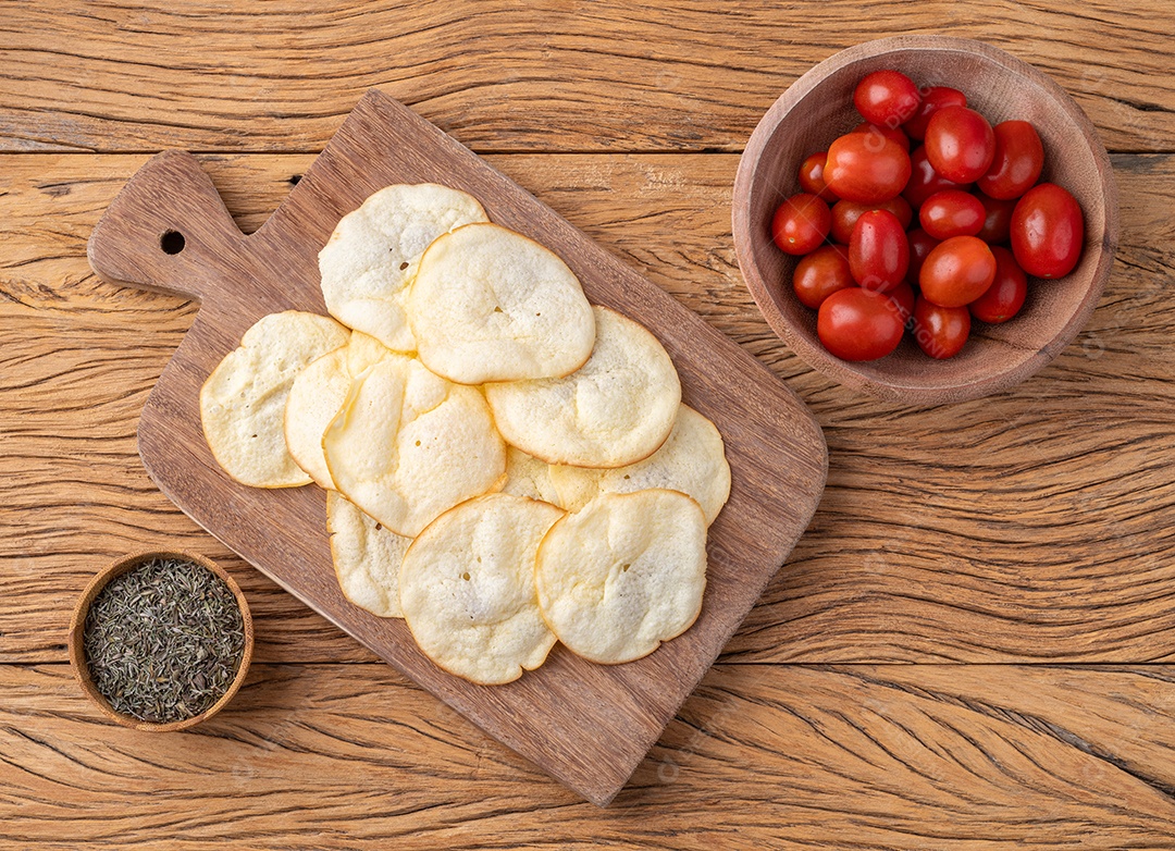 Lascas de queijo provolone defumado em uma tigela com tomate cereja e orégano sobre a mesa de madeira.