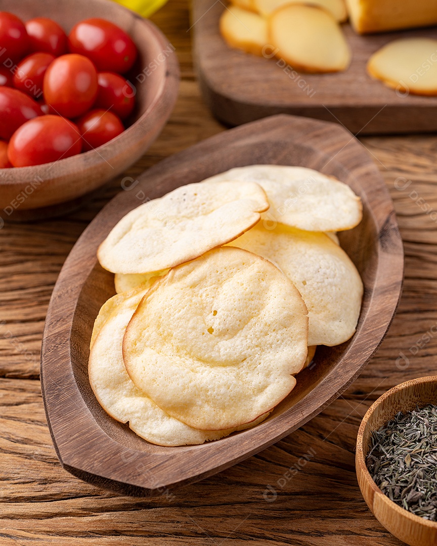Lascas de queijo provolone defumado em uma tigela com tomate cereja e orégano sobre a mesa de madeira.