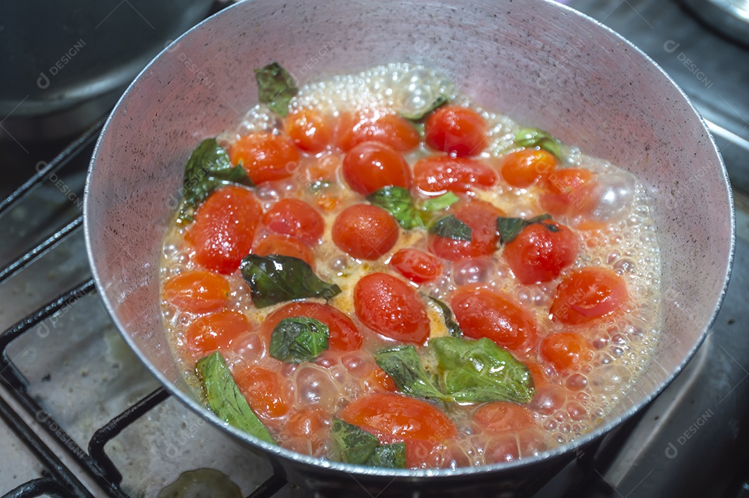 tomate cereja em uma panela sendo cozido com mangericão para fazer molho de tomate natural