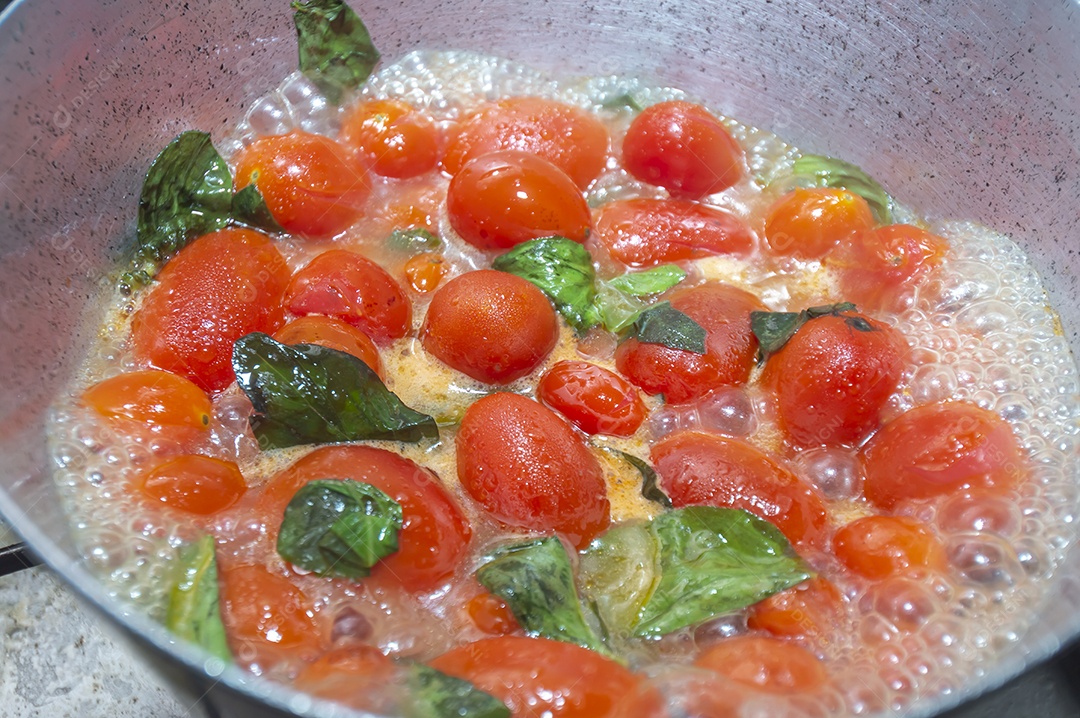 tomate cereja em uma panela sendo cozido com mangericão para fazer molho de tomate natural