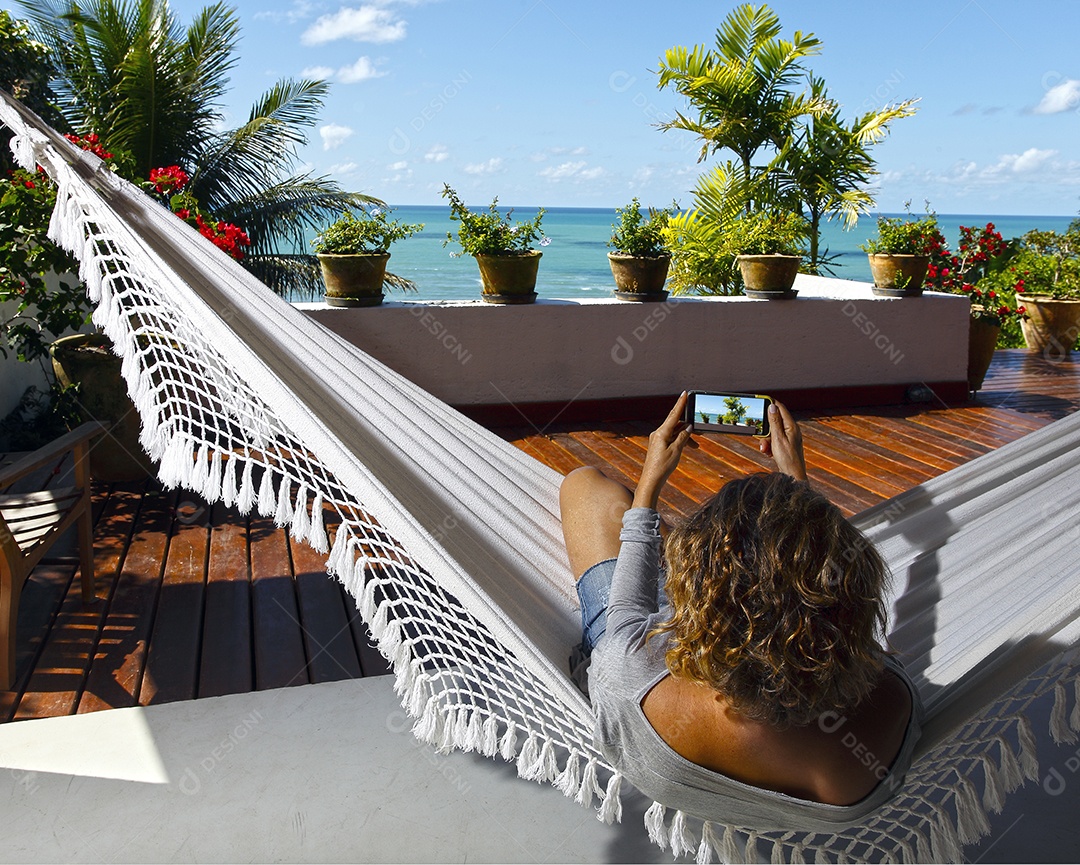 Uma mulher deitada numa rede e mexendo ao celular