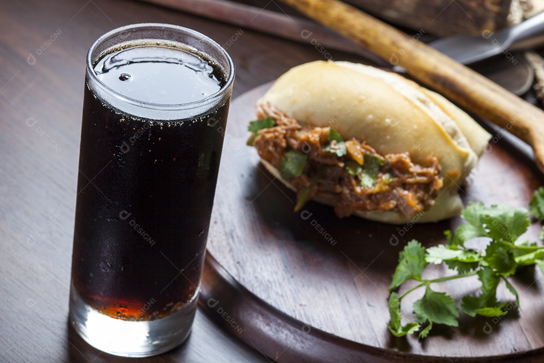 Pão recheado com carne e folhas e copo de refrigerante ao lado