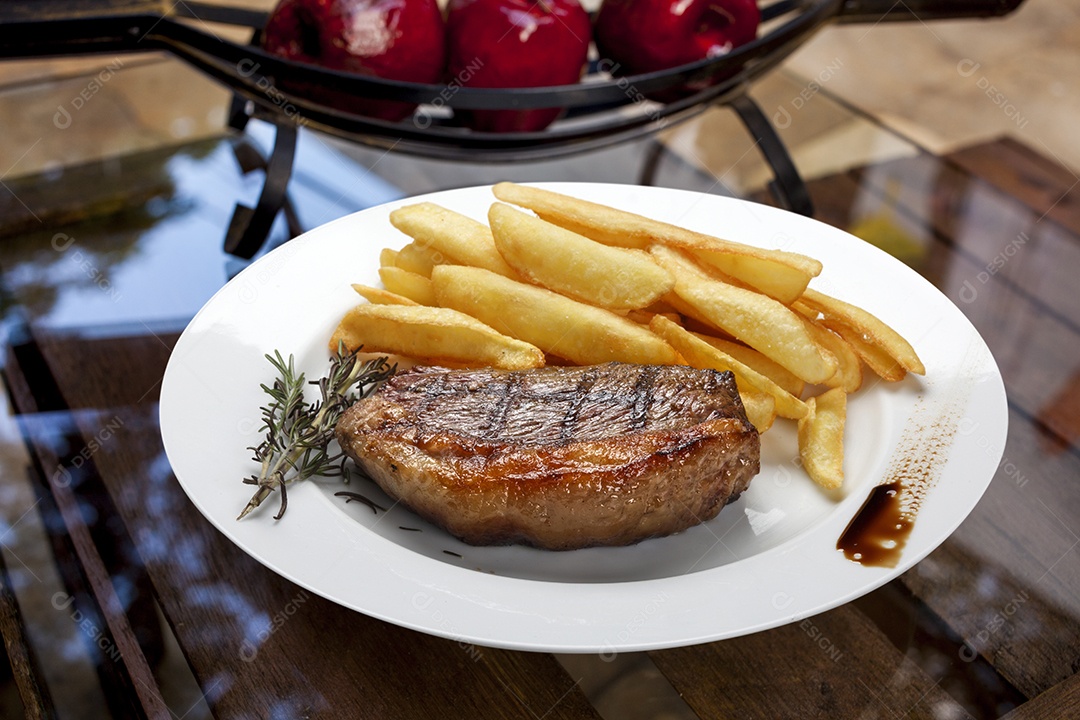 Bife de picanha com batatas fritas sobre mesa de vidro