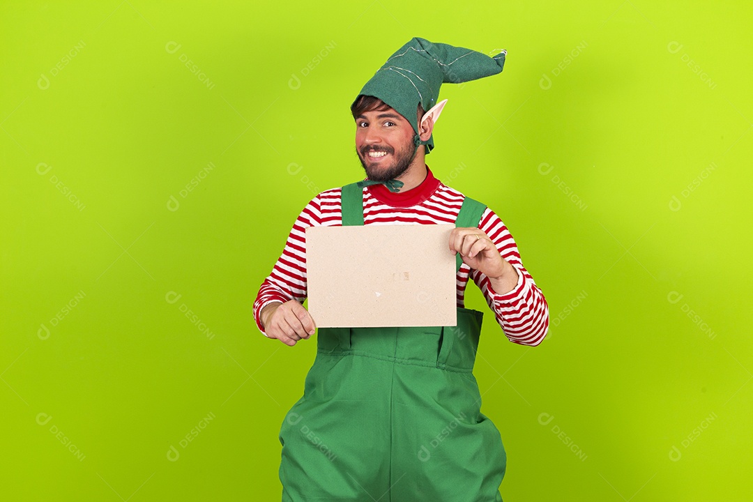 Homem com fantasia de duende segurando placa branca em fundo verde