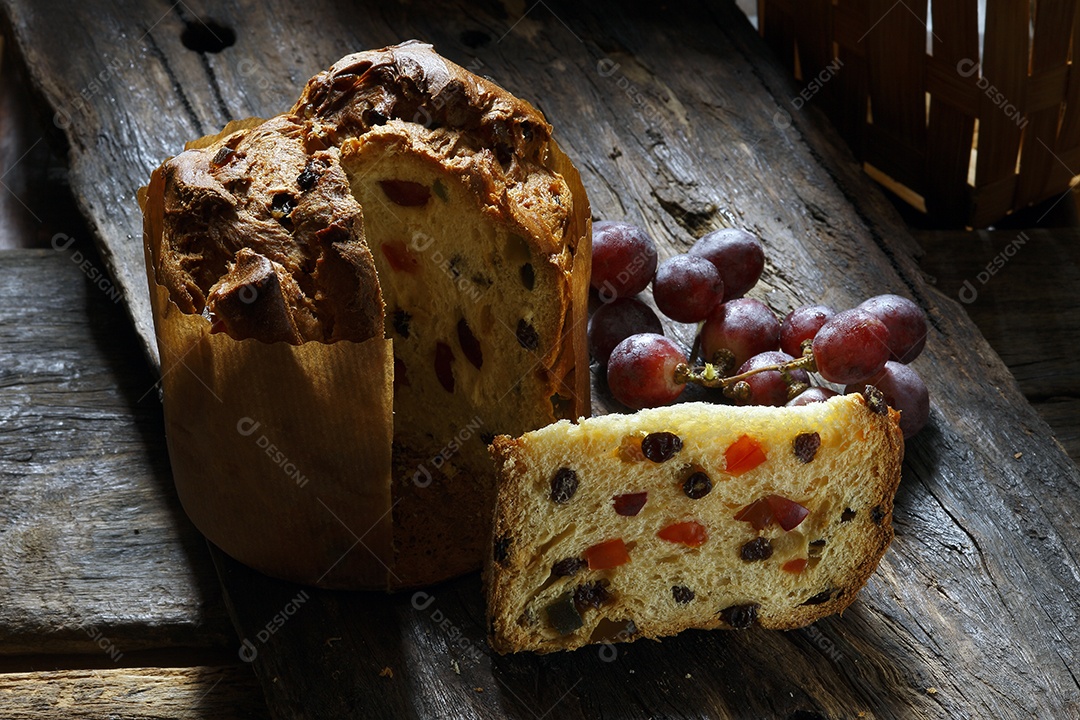 Panetone com frutas e uvas ao lado sobre uma mesa de madeira