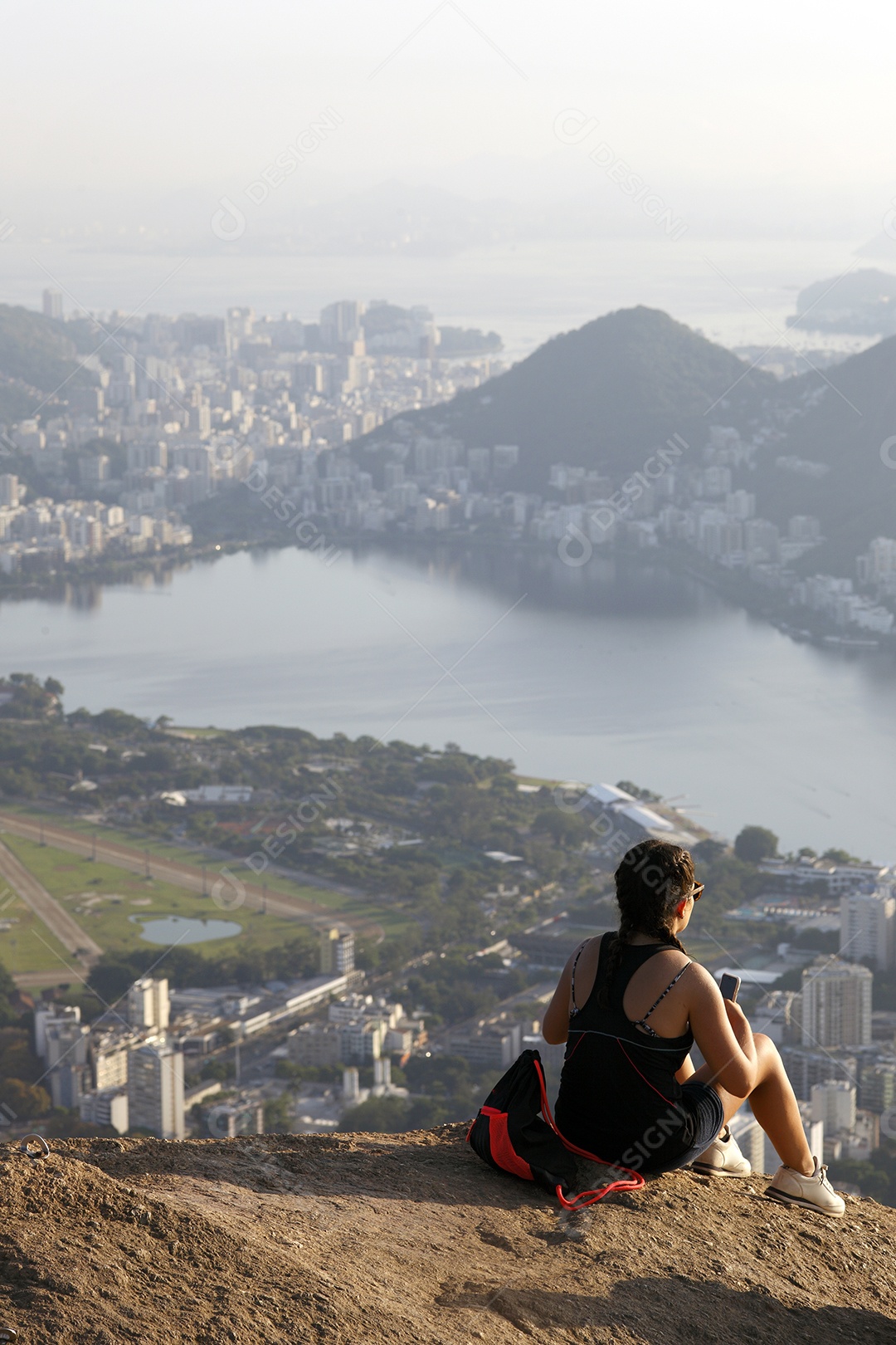 Mulher sentada no morro apreciando vista para o mar
