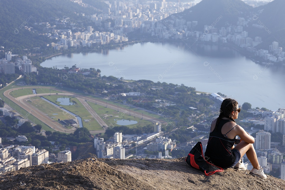 Mulher sentada no morro apreciando vista para o mar