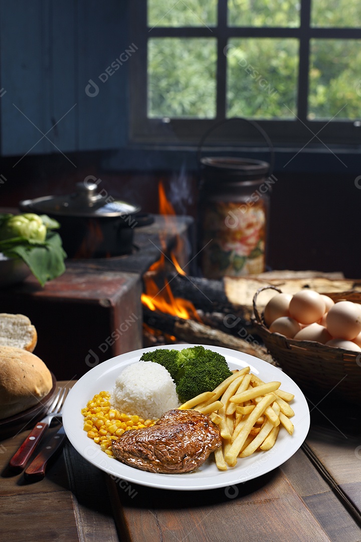 Bife grelhado com batata e arroz em um prato sobre mesa de madeira