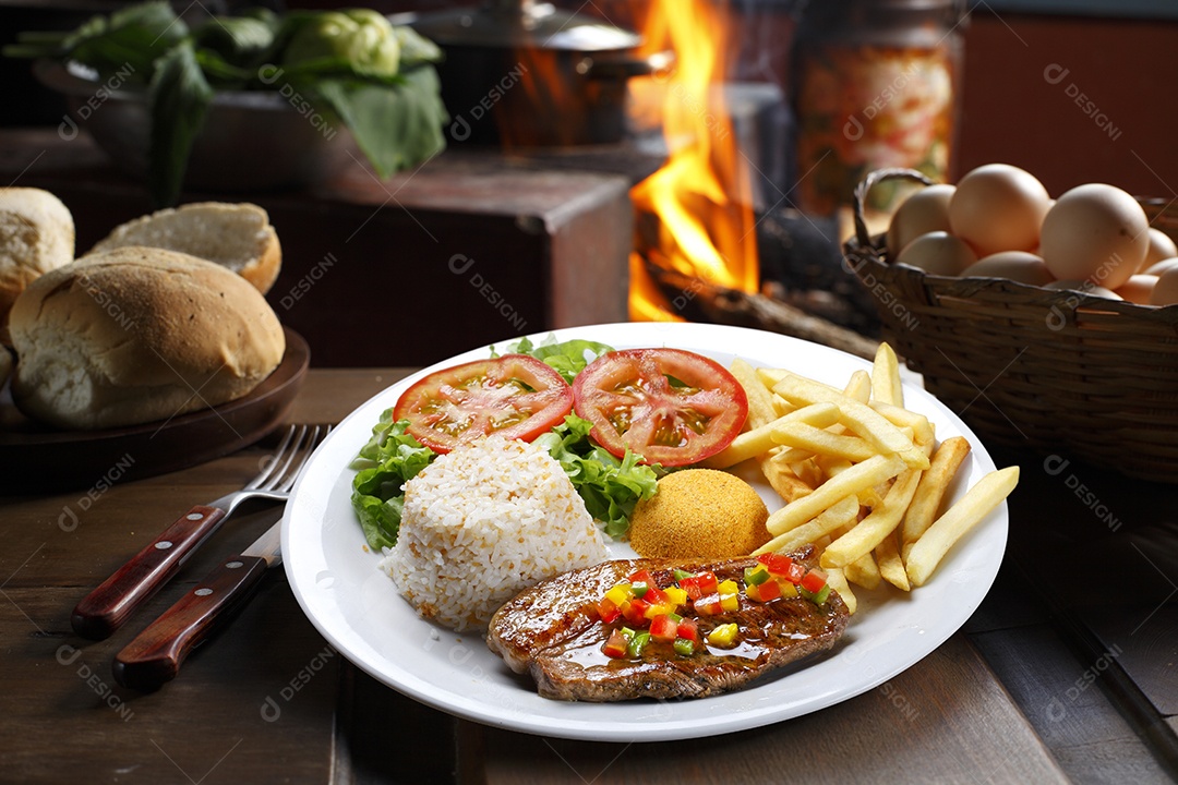 Bife grelhado com batata e arroz em um prato sobre mesa de madeira