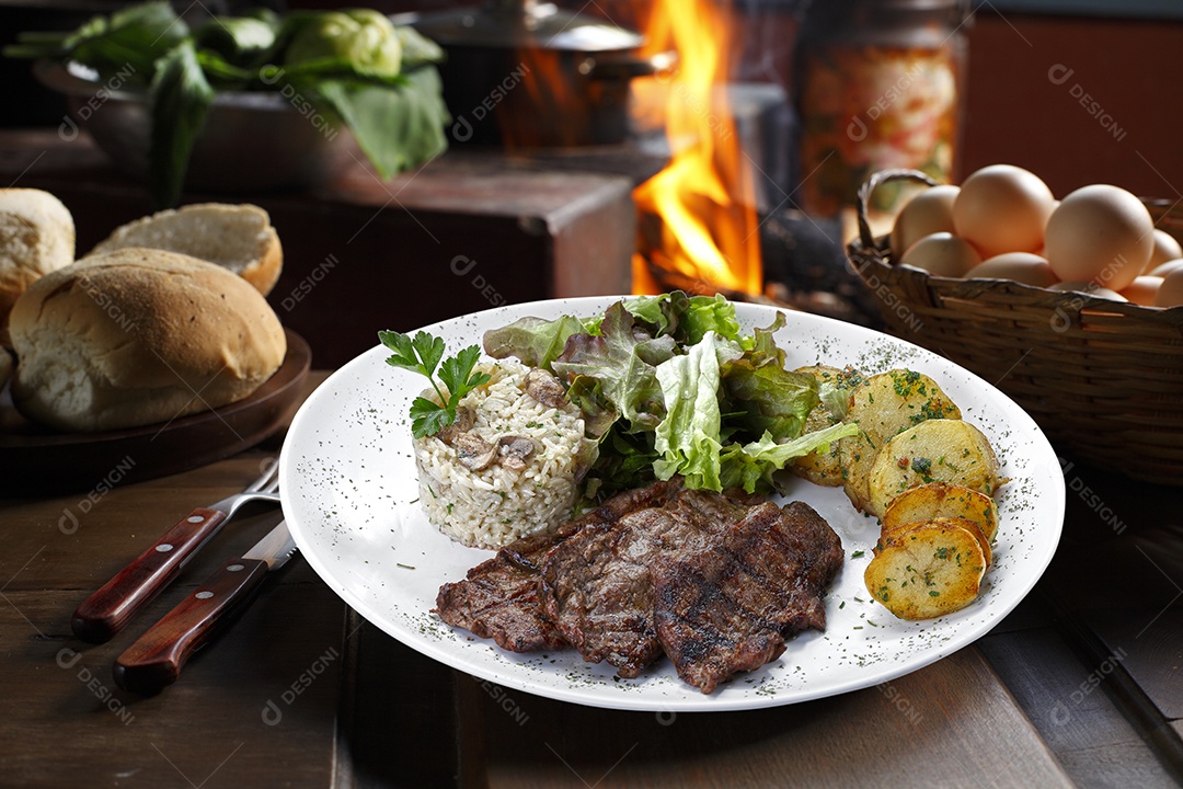 Bife grelhado com batata e arroz em um prato sobre mesa de madeira