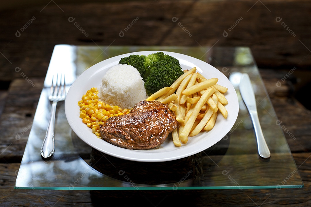 Bife grelhado com batata e arroz em um prato sobre mesa de madeira
