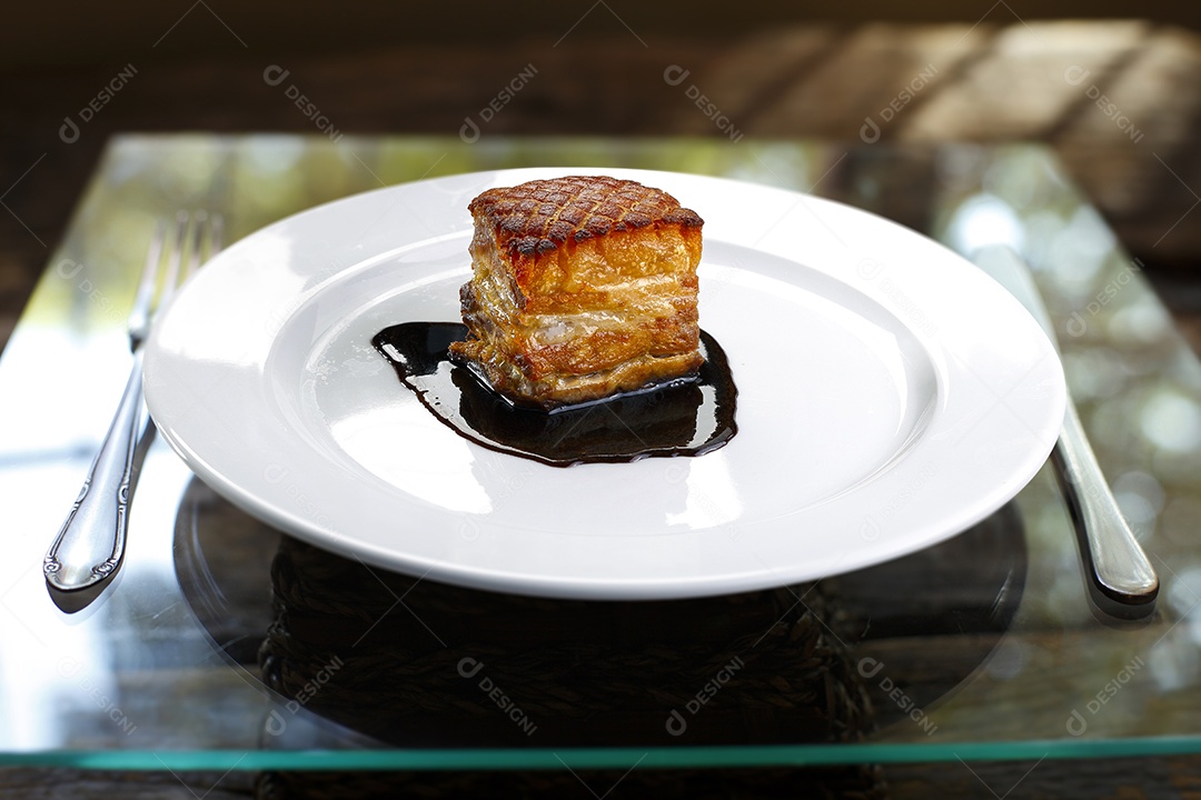 Barriga de porco assada em um prato sobre mesa de vidro