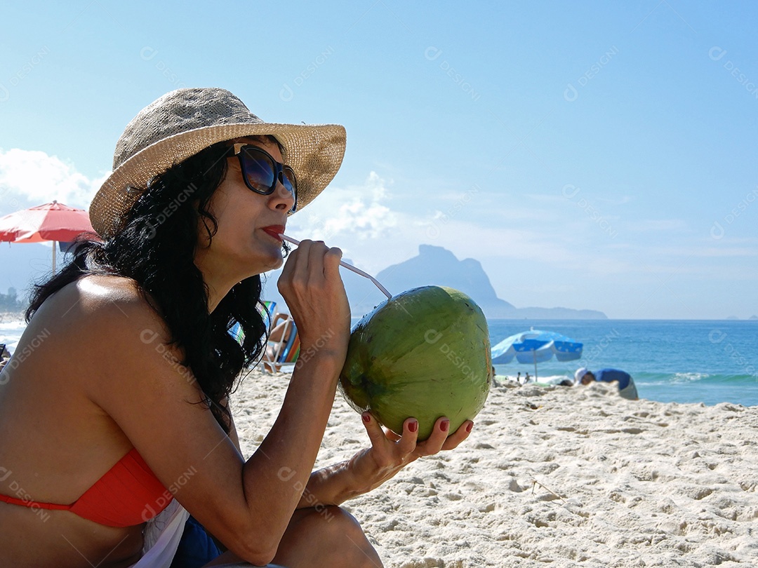 Mulher na praia bebendo água de coco no Rio de Janeiro