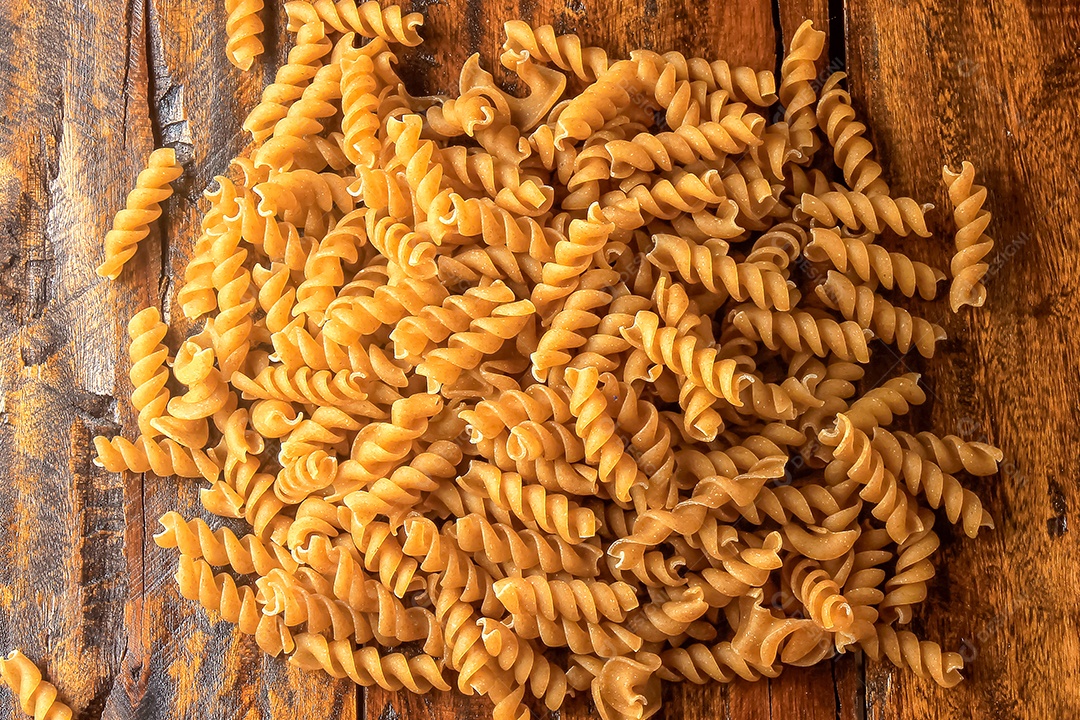 Massa fusilli crua de grãos integrais em tecido rústico sobre mesa de madeira. Fechar-se