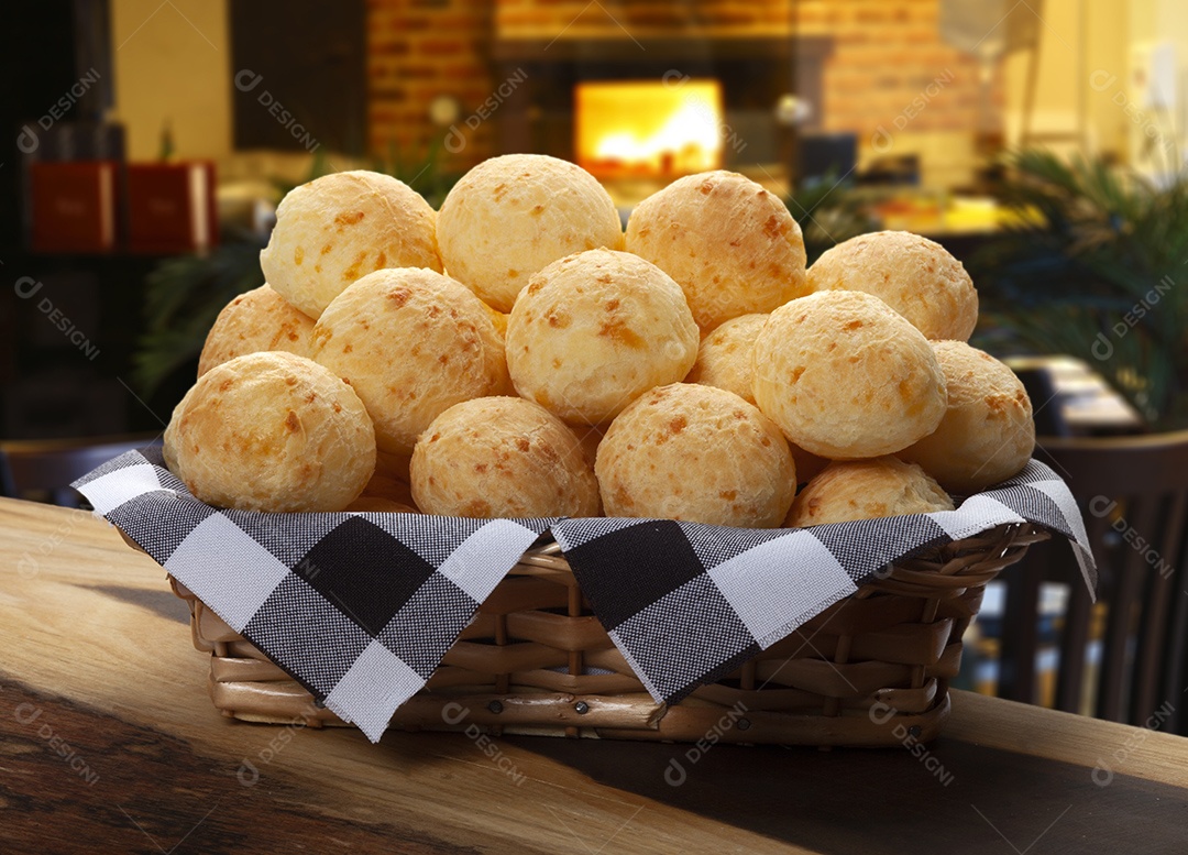 Cesta de vime com pães de queijo sobre mesa de madeira