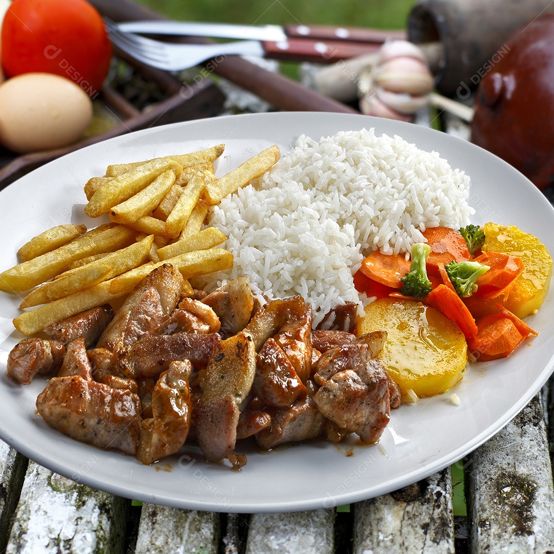 Carne de porco com arroz e batatas sobre mesa de madeira