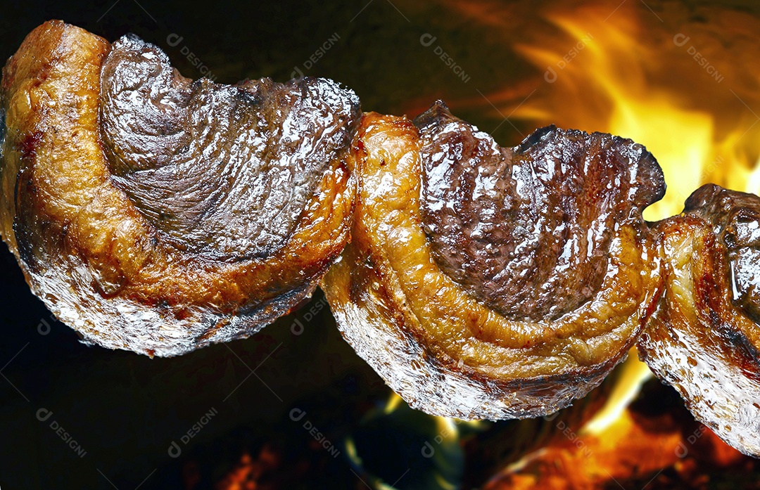 Espeto de picanha assado com brasa ao fundo