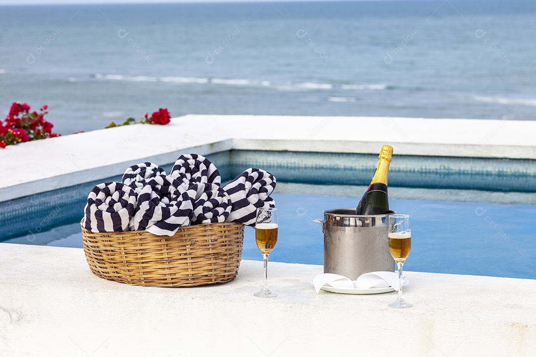 Piscina com vista para o mar com cesta de toalhas e champanhe