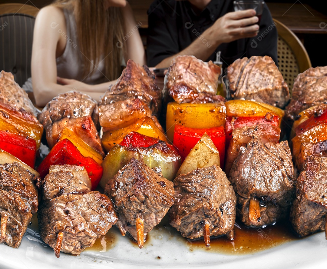 Casal comendo espetinhos de carne com legumes