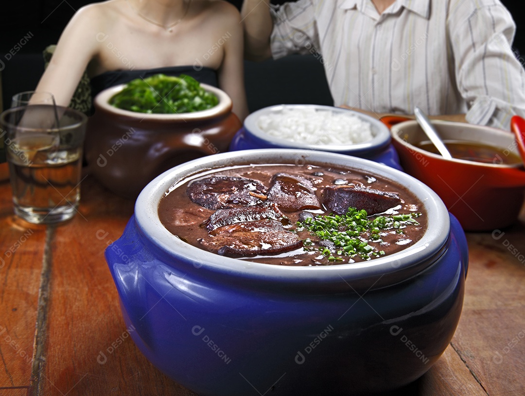Feijoada deliciosa com guarnições sobre mesa de madeira