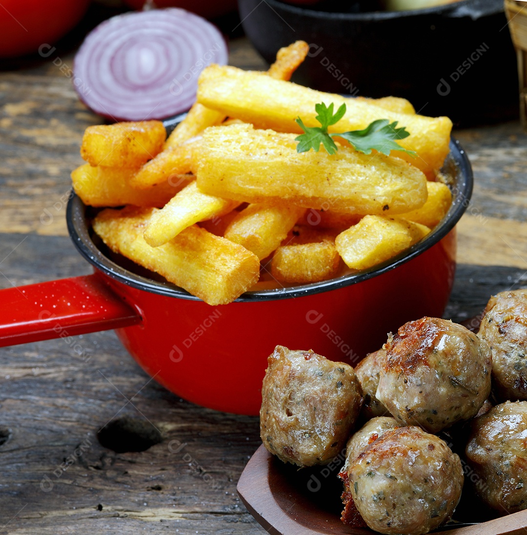 Mandioca frita e almôndega em tijela sobre mesa de madeira