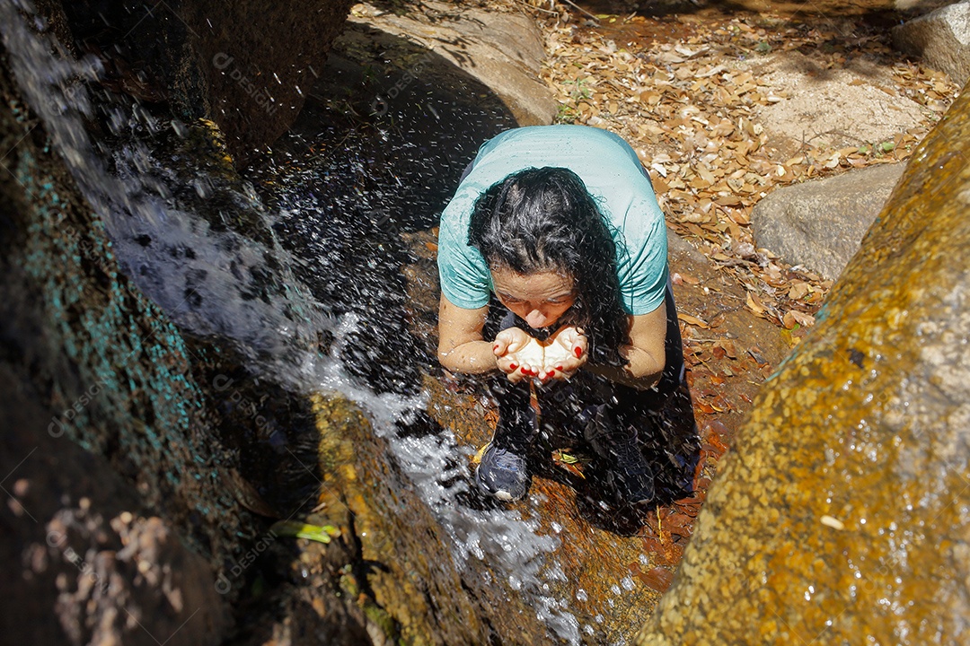 Mulher bebendo água em um riacho cristalino
