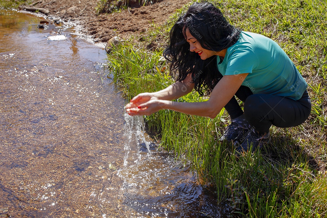 Mulher bebendo água em um riacho cristalino