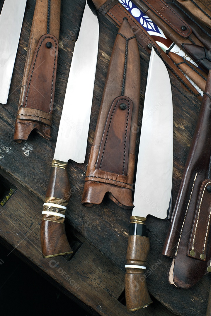 Facas afiadas com bainha de couro sobre tábua de madeira