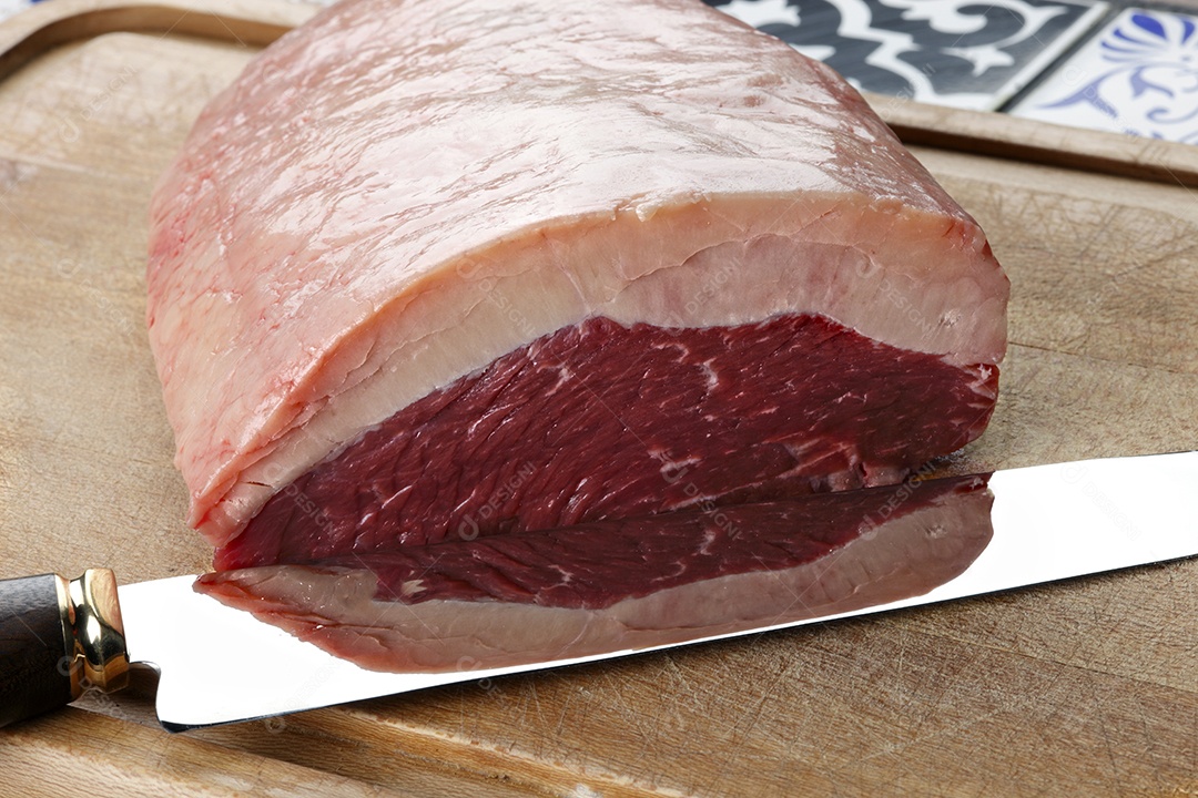 Peça de carne com gordura e faca sobre tábua de madeira