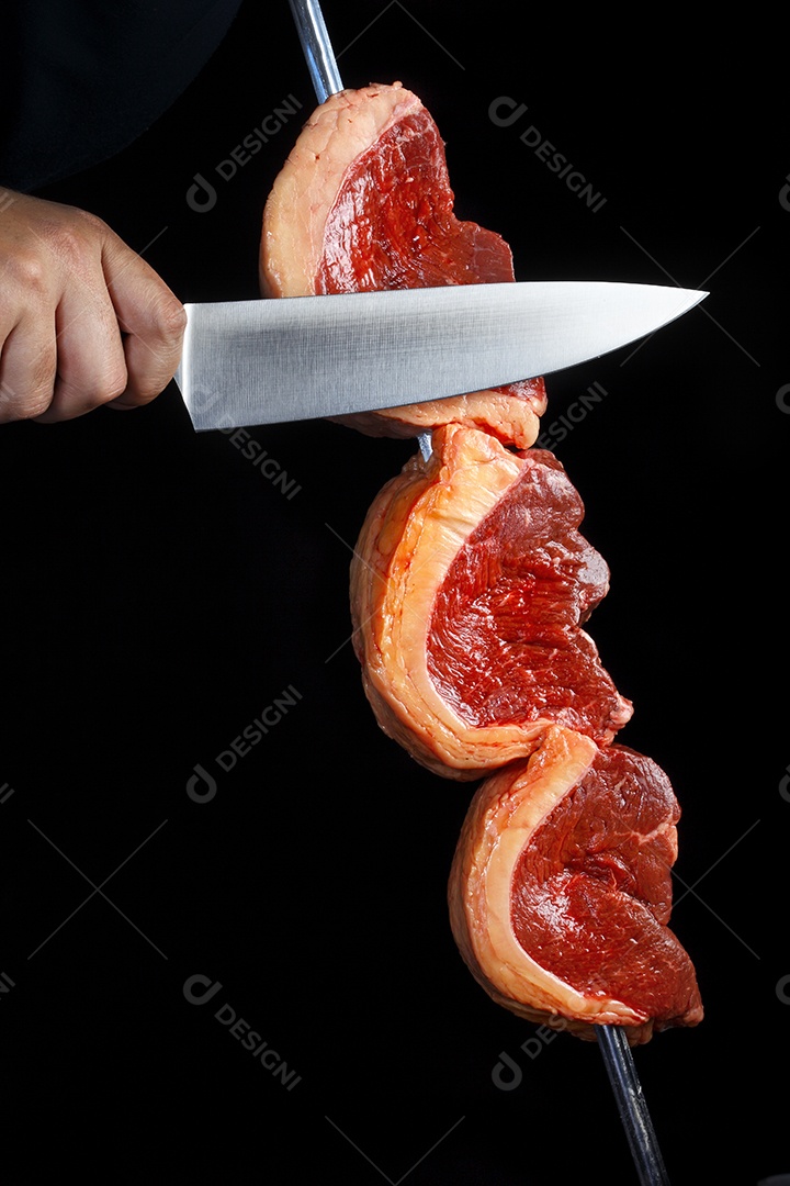 Espeto de carne crua e mão cortando