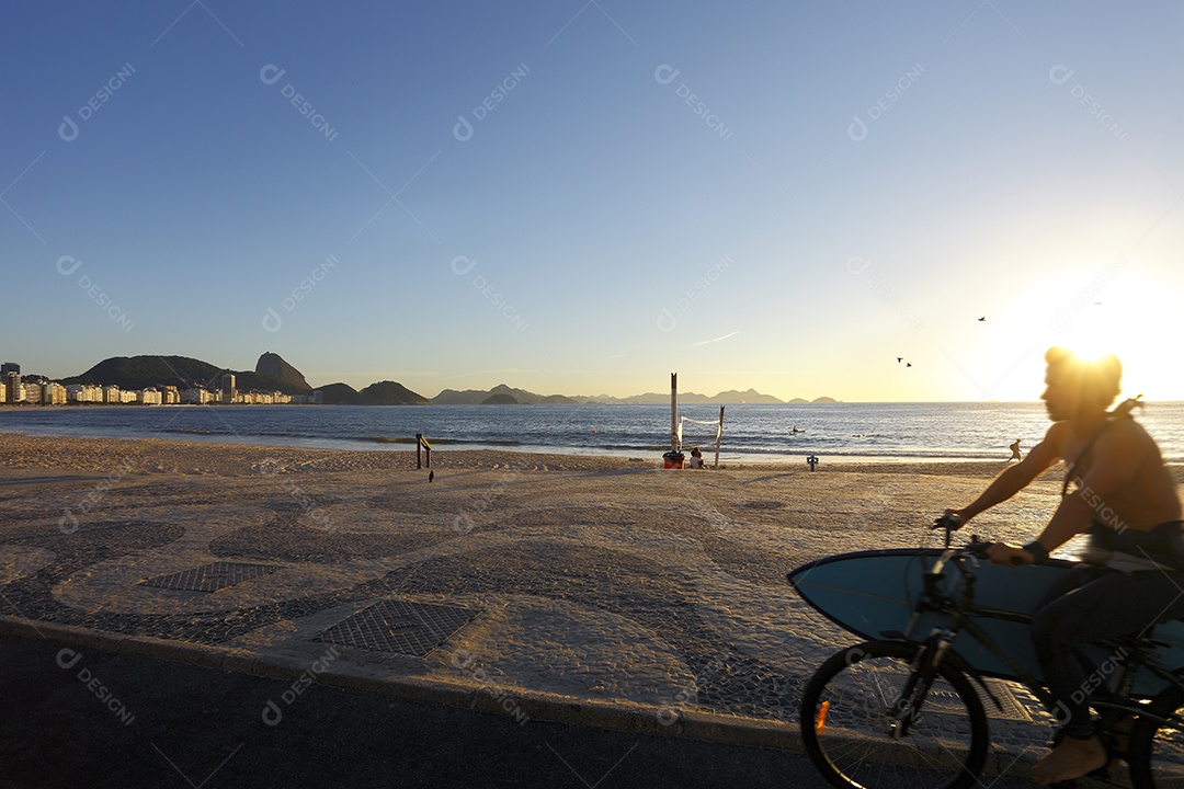 Ciclista segurando uma prancha na praia de copacabana