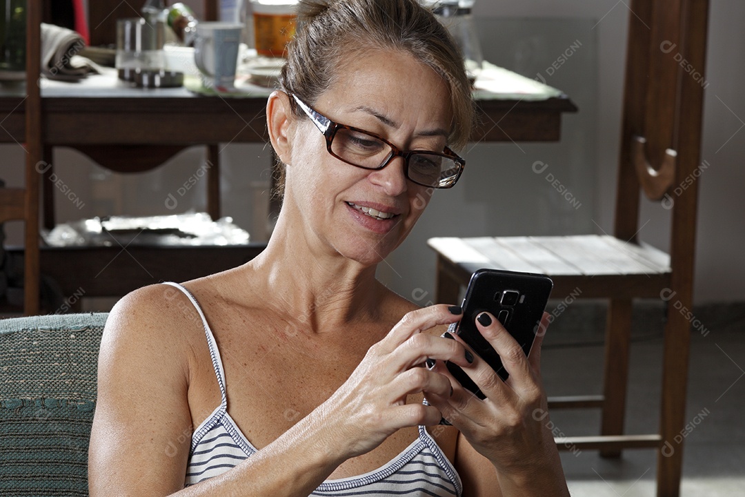 Mulher de cerca de 50 anos deitada vendo o celular