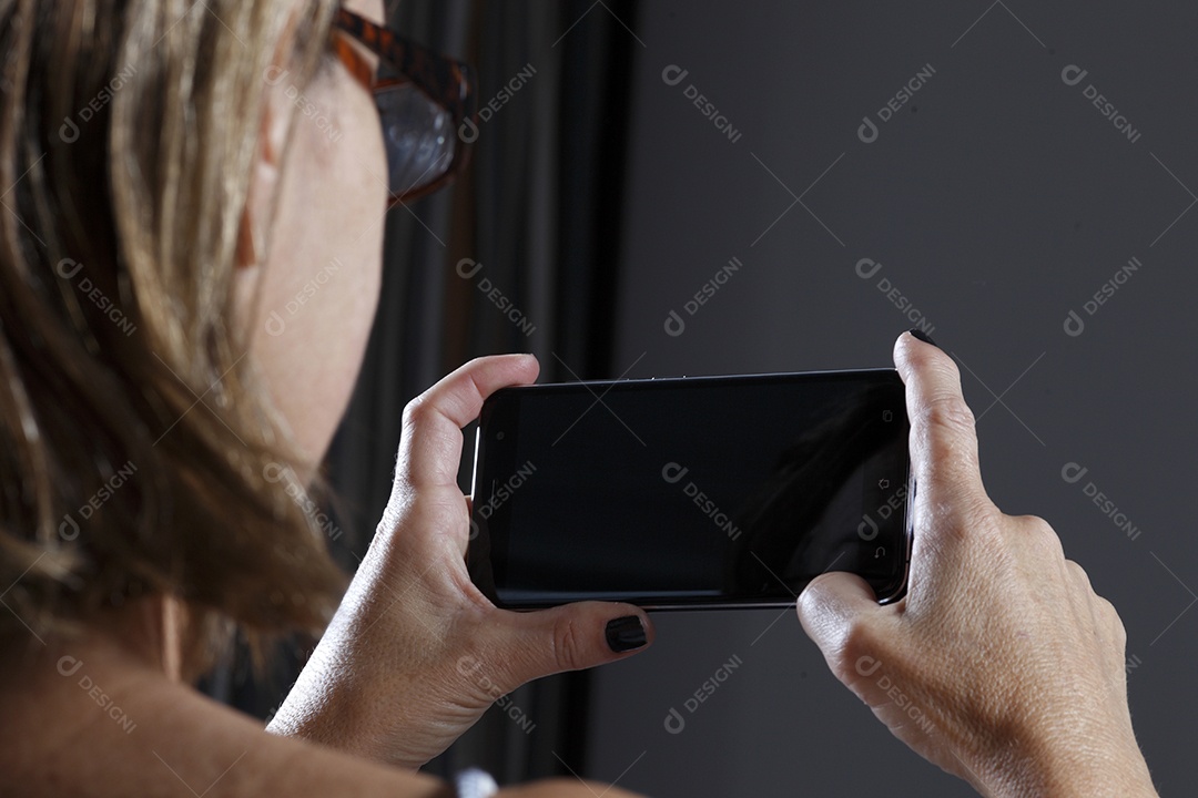 Mulher de cerca de 50 anos deitada vendo o celular