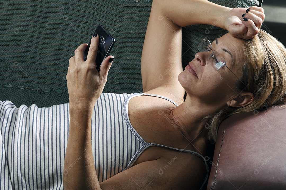 Mulher de cerca de 50 anos deitada vendo o celular