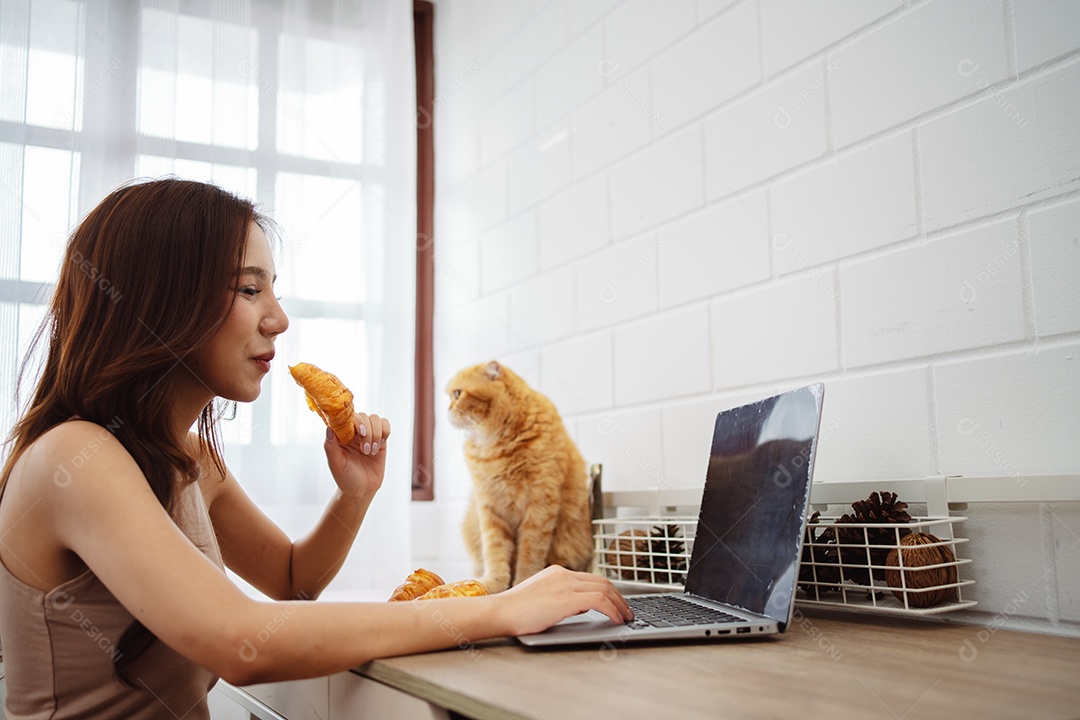 Mulher jovem asiática feliz trabalhando com computador portátil com gato bonito durante o dia de manhã.