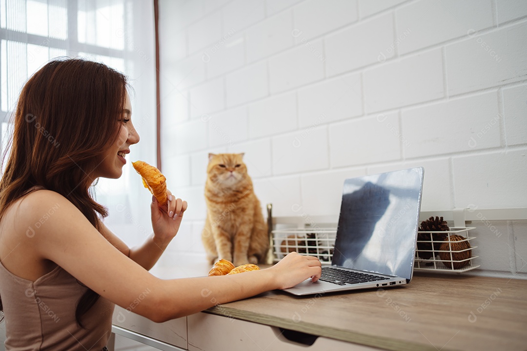 Mulher jovem asiática feliz trabalhando com computador portátil com gato bonito durante o dia de manhã.