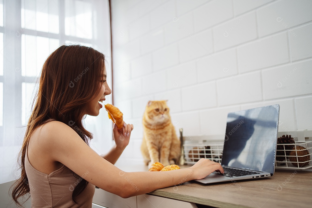 Mulher jovem asiática feliz trabalhando com computador portátil com gato bonito durante o dia de manhã.