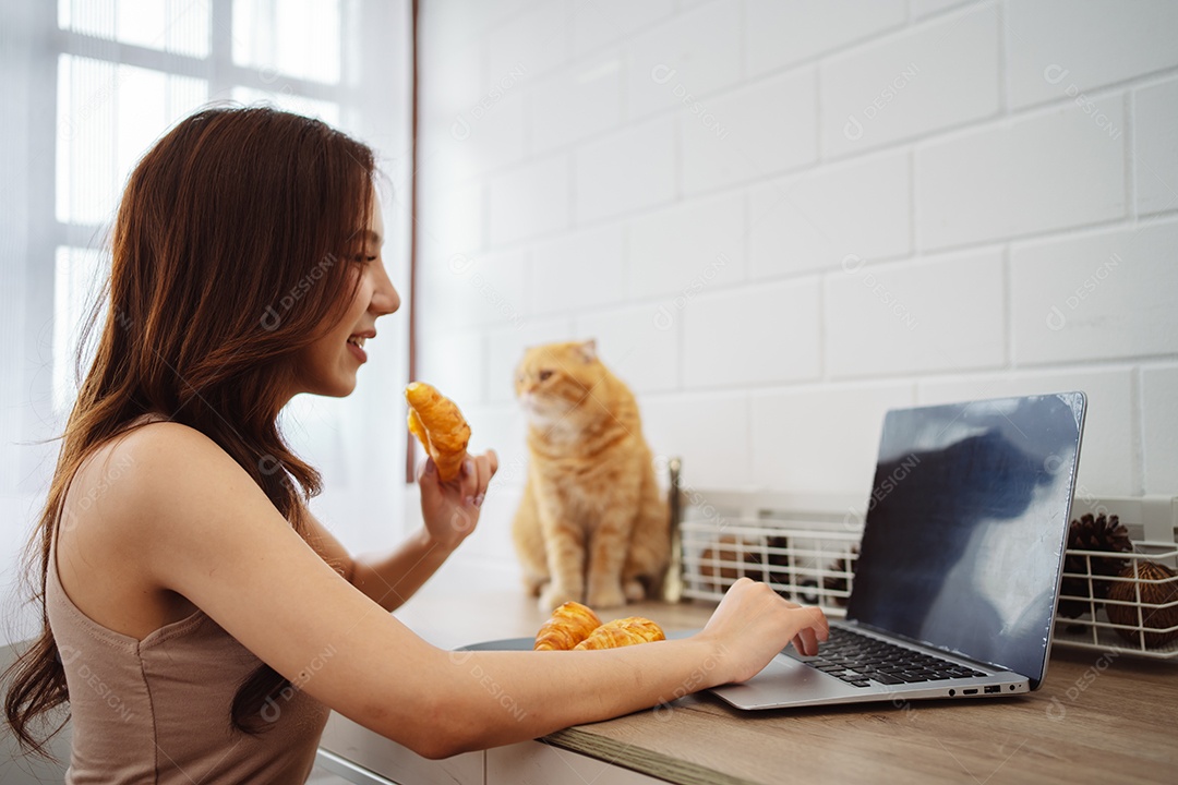 Mulher jovem asiática feliz trabalhando com computador portátil com gato bonito durante o dia de manhã.
