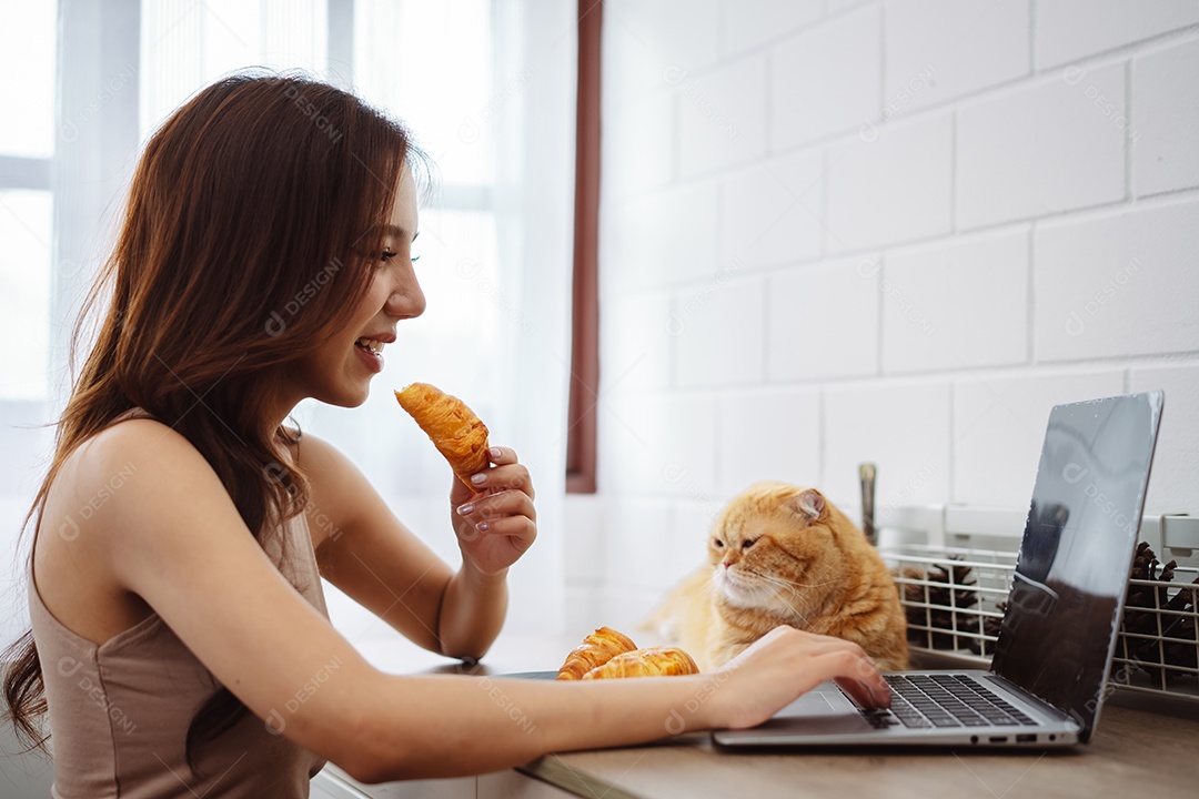 Mulher jovem asiática feliz trabalhando com computador portátil com gato bonito durante o dia de manhã.