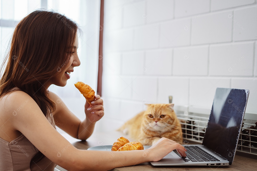 Mulher jovem asiática feliz trabalhando com computador portátil com gato bonito durante o dia de manhã.