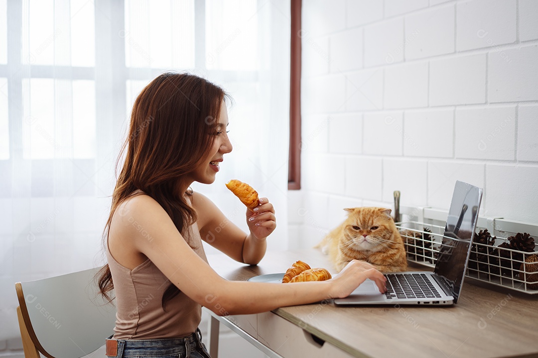 Mulher jovem asiática feliz trabalhando com computador portátil com gato bonito durante o dia de manhã.
