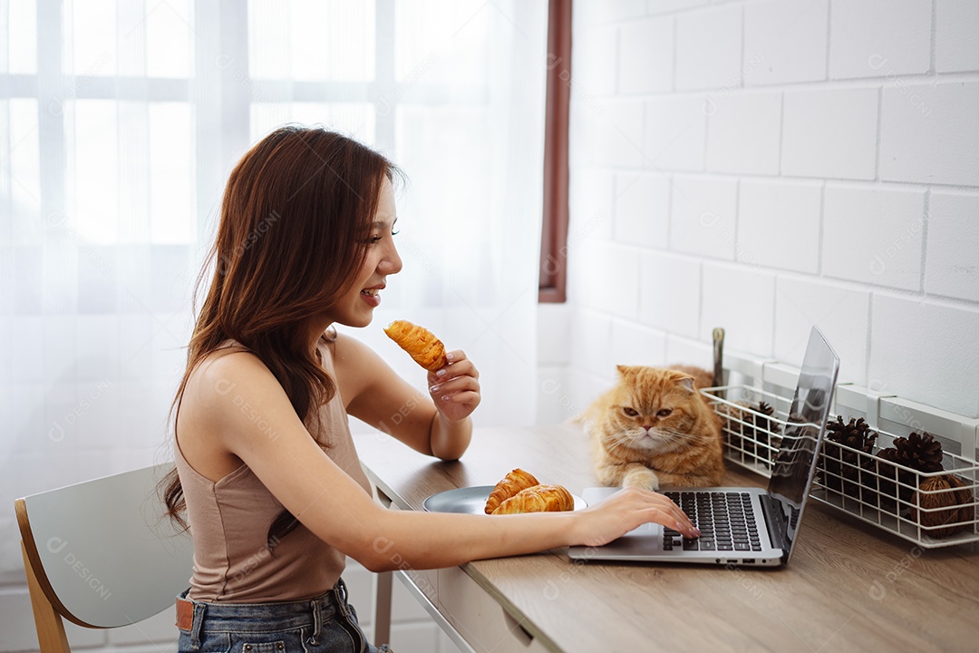 Mulher jovem asiática feliz trabalhando com computador portátil com gato bonito durante o dia de manhã.