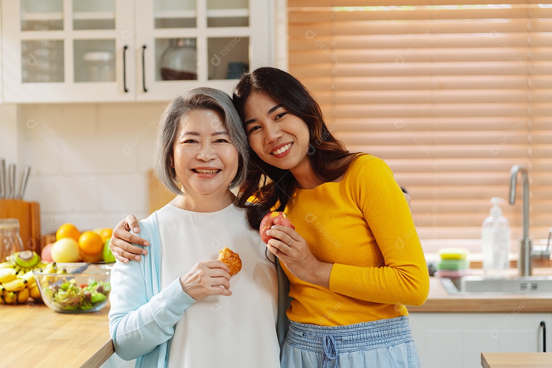 Filha de mulher asiática feliz abraçando mãe sênior na cozinha