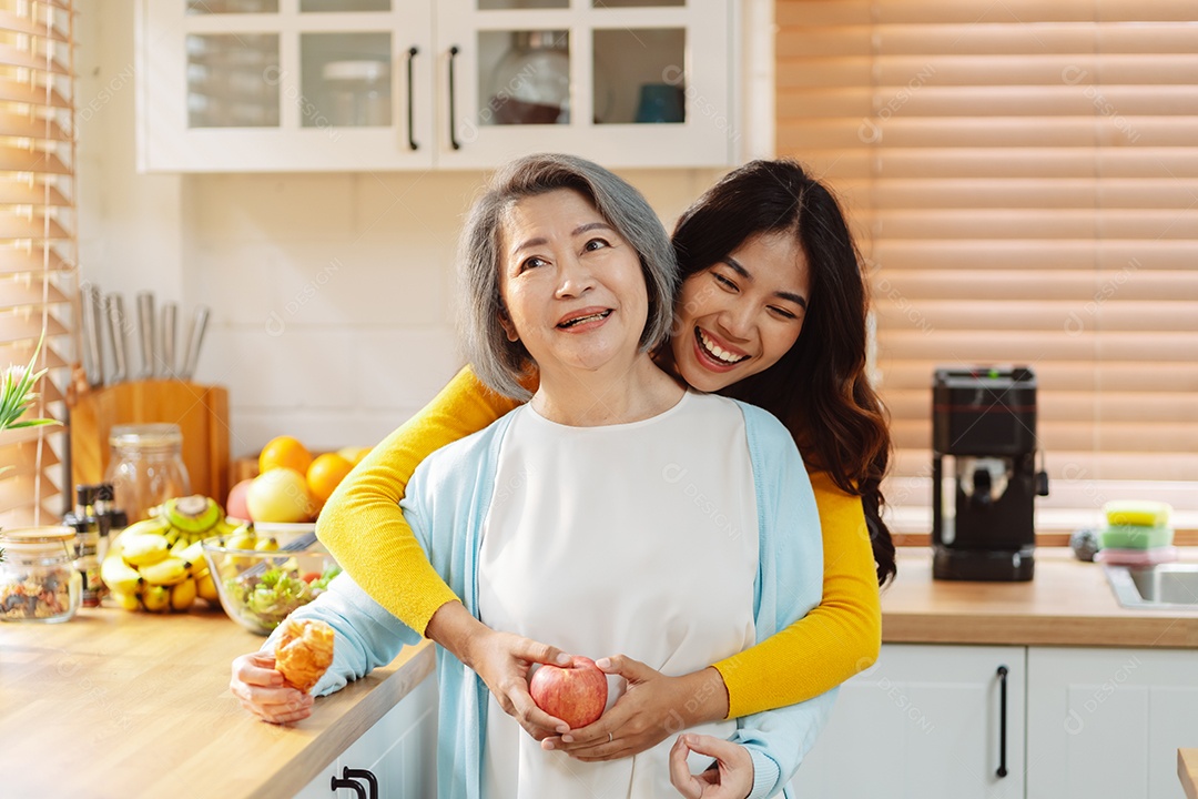 Filha de mulher asiática feliz abraçando mãe sênior na cozinha