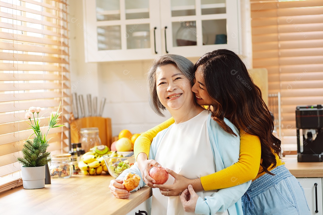 Filha de mulher asiática feliz abraçando mãe sênior na cozinha