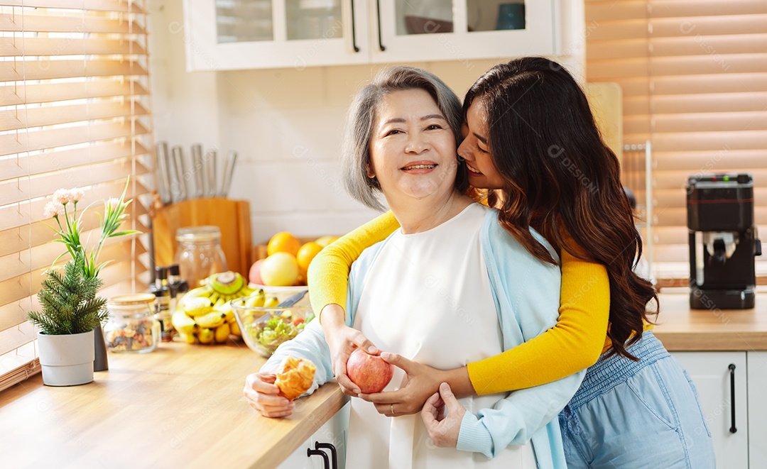 Filha de mulher asiática feliz abraçando mãe sênior na cozinha