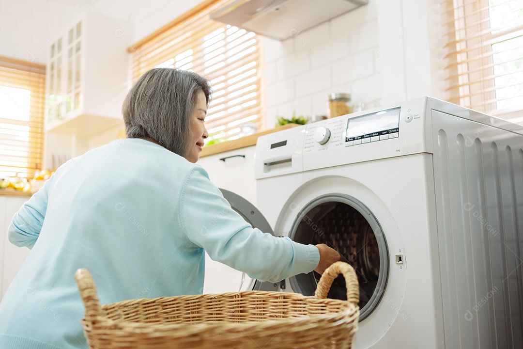 Mulher sênior asiática carregando roupas para a máquina de lavar.