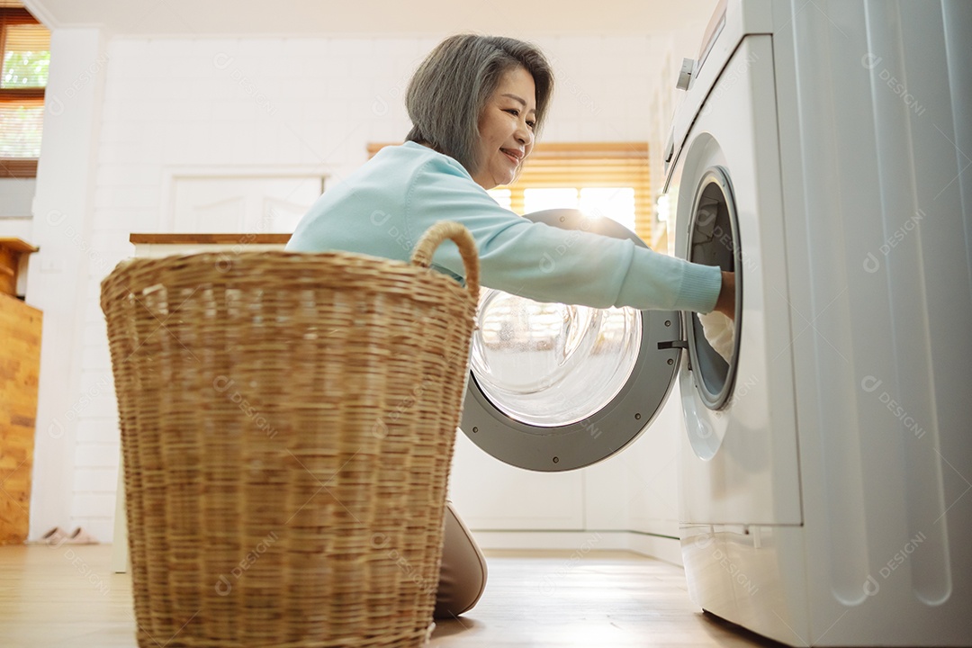 Mulher sênior asiática carregando roupas para a máquina de lavar.