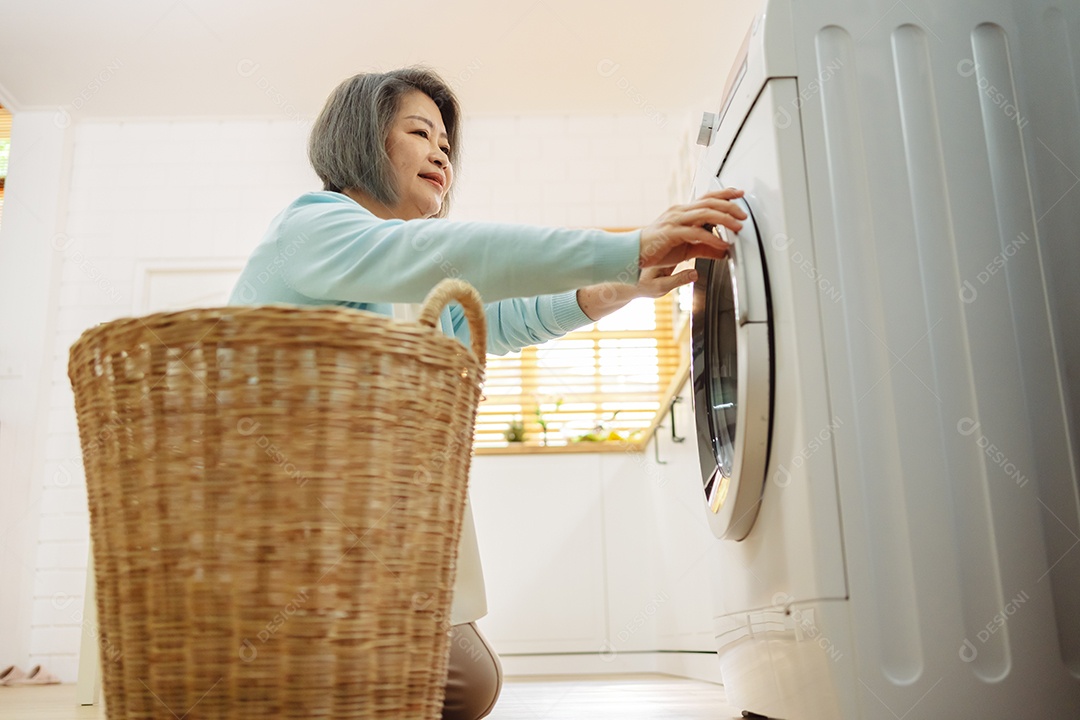 Mulher sênior asiática carregando roupas para a máquina de lavar.